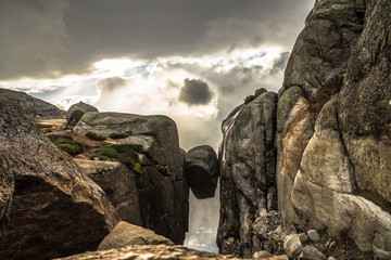 Rock stuck between two mountains with cloudy sky behind in Norway, Kjeragbolten 