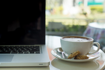 A cup of coffee in a white cup and computer labtop on mable tabl