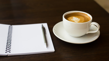Coffee cup and notebook on grunge wooden background.