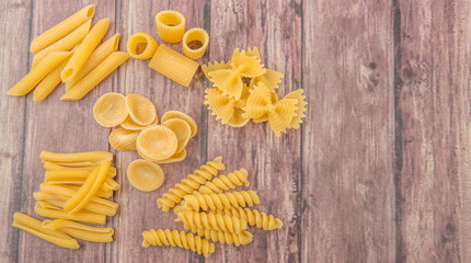 Assortment of different shape pastas over wooden background