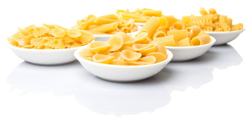 Dried pasta variety in shapes in white bowl over white background