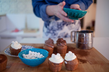 girl decorates cupcakes, holding  plate, muffins and  plate of ingredients for decoration on the table