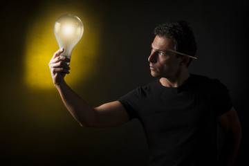 Concetto di creatività e business : uomo tiene in mano una lampadina accesa. Sfondo nero con luce...