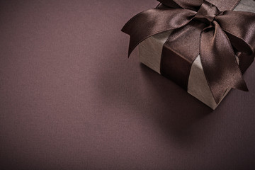 Present box with tied ribbon on brown background holidays concep