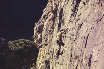 Man climbing a mountain alone, with a dark valley in the background.