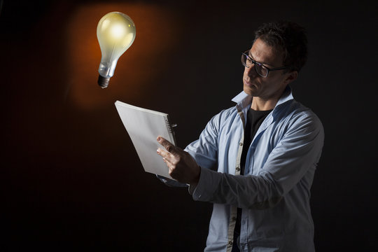 Concetto di ingegno, idea e creativit&agrave; : uomo d'affari scrive su un quaderno. Sfondo con lampadina accesa