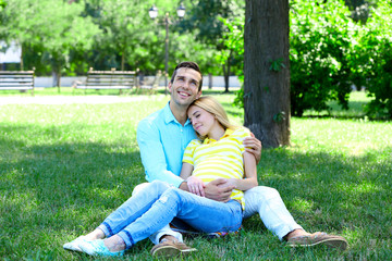 Naklejka na ściany i meble Young pregnant woman with husband sitting on green grass in park