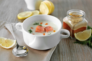 Delicious salmon cream soup on wooden table, which served with sliced lemon and spices