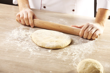 Hands rolling dough for pizza on the wooden table, close-up
