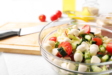 Tasty salad in glass dish on color wooden table background