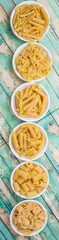 Various dried pasta variety and shapes in white bowl over wooden background
