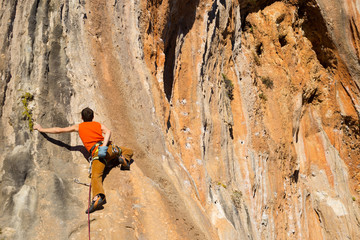 Young male climber hanging by a cliff.