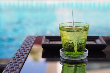 A green glass of drinking water on a table beside swimming pool 