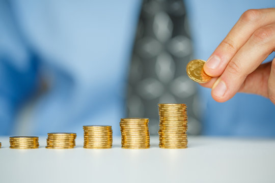 Male hand stacking gold coins into increasing columns