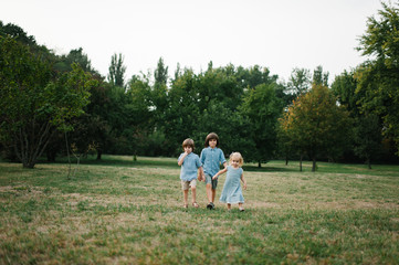 Three kids walking on grass in park on summer afternoon in park and playing to each other