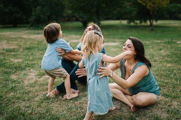 Obraz premium Happy young hipster family having fun while running, bowl, rising up, piggyback ride their children in park on summer sunset 