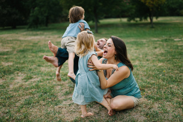 Happy young hipster family having fun while running, bowl, rising up, piggyback ride their children in park on summer sunset
