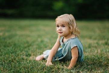 Portrait of a child sitting on grass on summer sunset afternoon and playing
