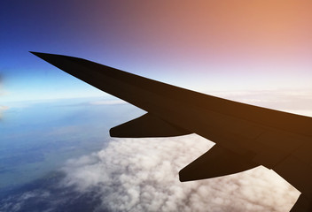Fototapeta na wymiar silhouette Airplane wing flying above clouds window view on sunset
