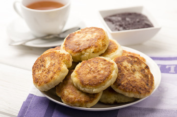 Cottage cheese pancakes with a cup of tea on the white wooden background.