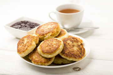 Cottage cheese pancakes with a cup of tea on the white wooden background.