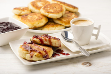 Cottage cheese pancakes with a cup of coffee on the white wooden background.