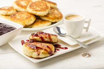 Cottage cheese pancakes with a cup of coffee on the white wooden background.