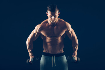 Fototapeta na wymiar Closeup of a muscular young man lifting dumbbells weights on dark background