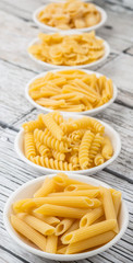 Various dried pasta variety and shapes in white bowl over wooden background