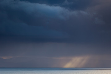 Fototapeta na wymiar Sunrays Through Dark Rainy Clouds over the Shore of Atlantic Ocean