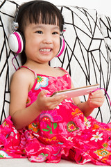 Chinese little girl on headphones holding mobile phone