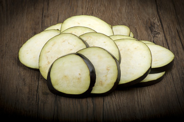 Aubergines eggplants and slices on wood background