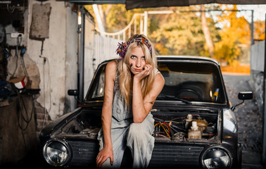 Fototapeta na wymiar young blonde girl with long hair is an auto mechanic in the garage with a lot of tools on the shelves holding wrenches