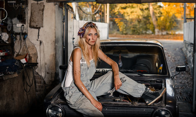 Plakat young blonde girl with long hair is an auto mechanic in the garage with a lot of tools on the shelves holding wrenches