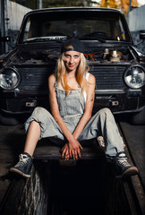 Obraz na płótnie Canvas young blonde girl with long hair is an auto mechanic in the garage with a lot of tools on the shelves holding wrenches