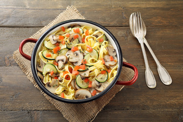 Pasta italiana con funghi zucchine e pomodoro su sfondo legno rustico