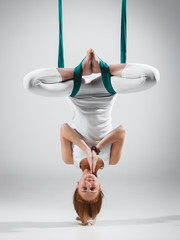 Young woman practices different inversion aerial yoga with a hammock in a white studio. Concept of...