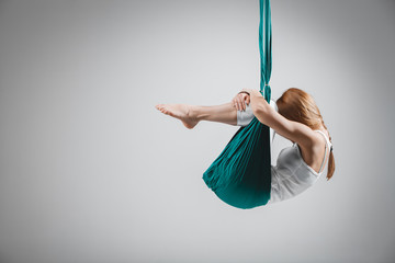 Young woman practices different inversion aerial yoga with a hammock in a white studio. Concept of...