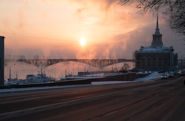 Здание речного вокзала и Коммунальный мост в городе Красноярск. Морозный закат солнца и поднимающийся пар от реки.