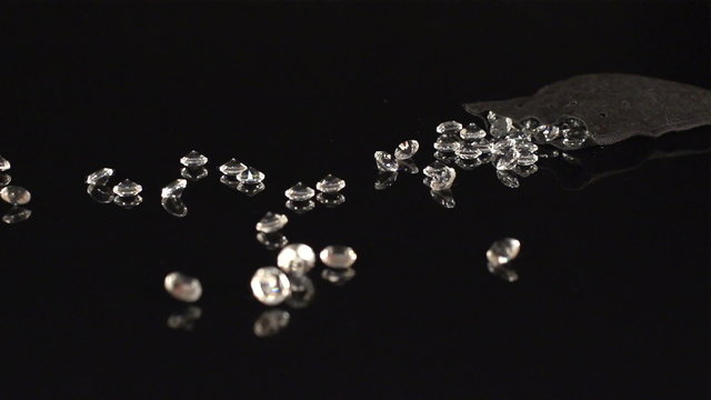 SUPER SLOW (240fps): A lot of a diamonds fall out from a pouch on a black table
