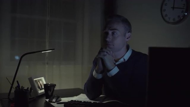 A praying or prayerful man works at a clean desk with a computer