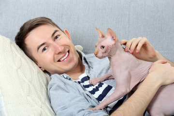 Young handsome man lies with cat on couch at home