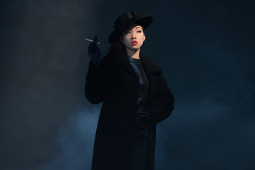 Retro 1940 asian fashion woman. Smoking cigarette. Wearing hat.