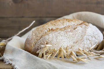Freshly baked homemade bread on a wooden table. Next to the bread wheat and oats ears. Rustic style. Closeup.