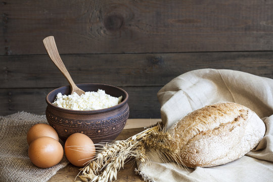 Rustic natural dairy products. Rustic natural dairy products cottage cheese and bread, eggs, onions and garlic of wheat on the old wooden background.