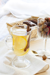 Fresh hot green tea in glass cup with lemon and cinnamon, chocolate cakes in basket and nuts and cinnamon in glass goblet.