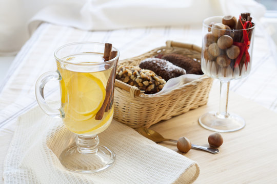 Fresh hot green tea in glass cup with lemon and cinnamon, chocolate cakes in basket and nuts and cinnamon in glass goblet.