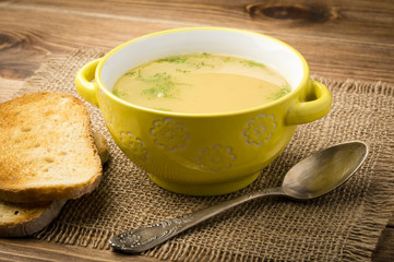 Peas soup in the yellow bowl on the wooden background.
