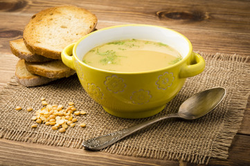 Peas soup in the yellow bowl on the wooden background.