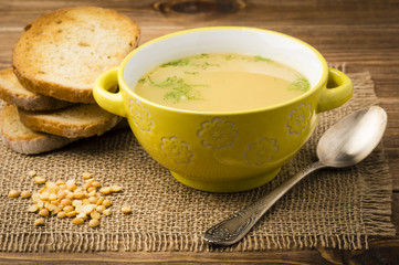 Peas soup in the yellow bowl on the wooden background.